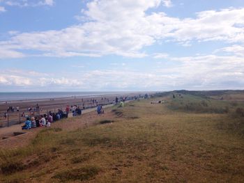 People relaxing on beach against cloudy sky