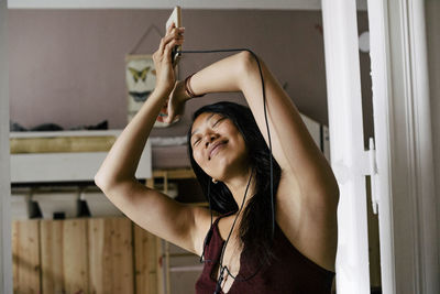 Carefree woman enjoying music through earphones at home