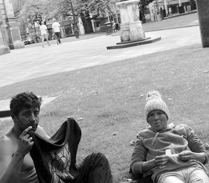 Portrait of friends sitting on sidewalk in city