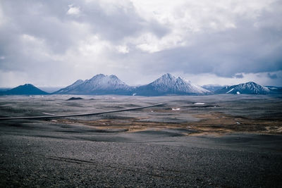 Scenic view of landscape and snowcapped mountains against cloudy sky