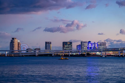 Sea by modern buildings against sky at dusk