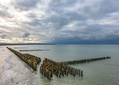 Wooden posts in sea against sky