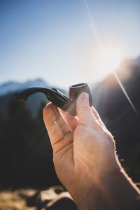 Cropped hand of man holding pipe cigarette against sky