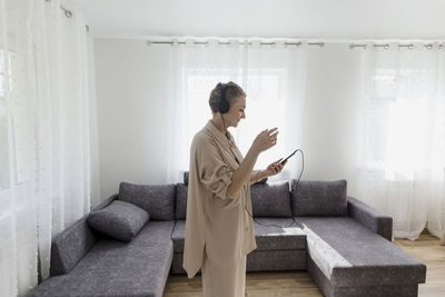 Mature woman wearing headphones listening to music at home