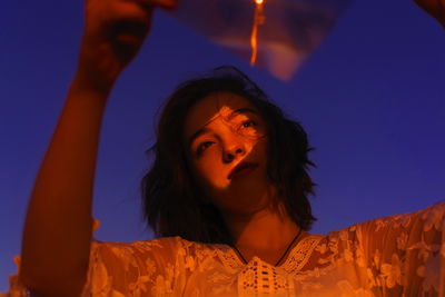 Young woman looking away while holding plastic with reflection on face against sky