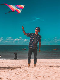 Full length of man holding kite standing on beach against sky