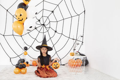 High angle view of boy sitting on pumpkin against wall during halloween