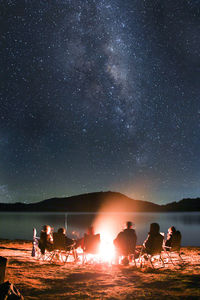 People sitting by sea against sky at night