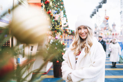 Young happy woman on shopping at christmas fair market in winter street decorated with lights