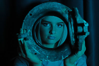 Close-up portrait of young woman wearing nose ring holding metal in dark