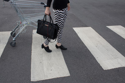Low section of woman with shopping cart walking on road