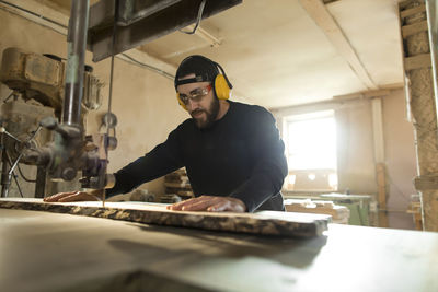 Woodworker sawing wood through bandsaw in workshop