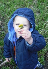 Portrait of baby boy holding flower on field