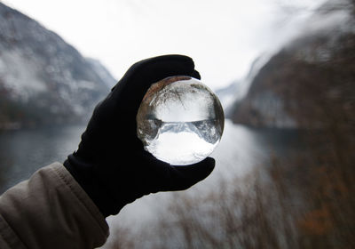 Close-up of hand holding crystal ball against lake during winter