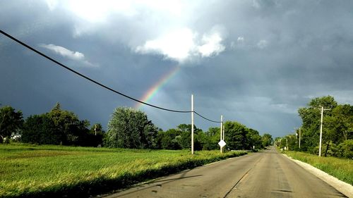 Road passing through field against cloudy sky