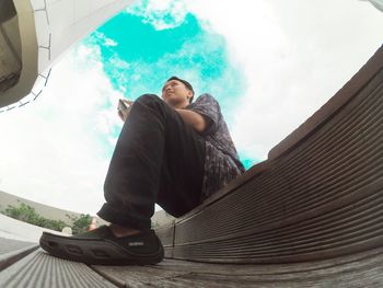 Low angle view of young man sitting against sky