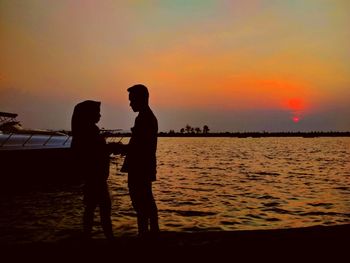 Silhouette men standing on beach against sky during sunset