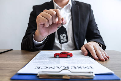 Midsection of man holding car key over papers and toy on table