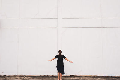 Full length rear view of woman with arms outstretched standing against wall