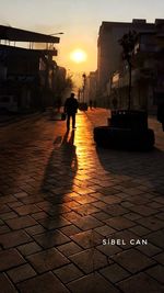 Silhouette man walking on footpath in city at sunset