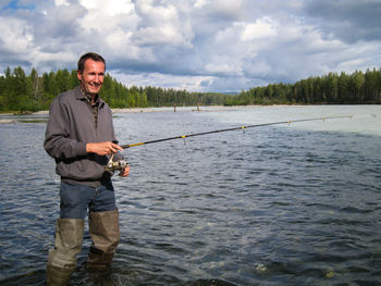 Portrait of man fishing in lake against sky