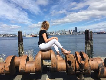 Young woman by retaining wall by sea against sky