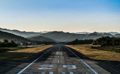 Empty road leading towards mountains against clear sky