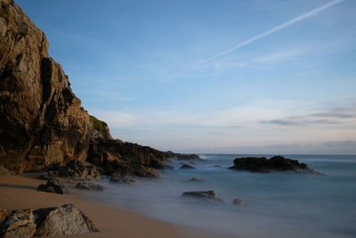 Ocean water foam on rock seacost with plane trail on sky