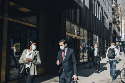 Businessman with female colleague talking while walking on footpath in city during pandemic