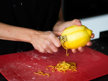 Midsection of woman peeling lemon at kitchen counter