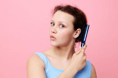 Portrait of young woman holding lollipop against pink background