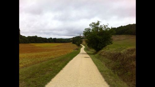Road passing through field against cloudy sky