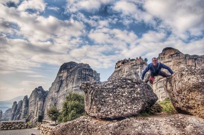 People on rocks by mountain against sky