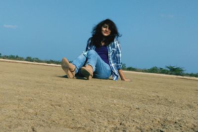 Woman sitting on sand against blue sky