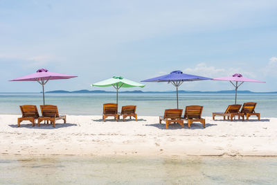 Lounge chairs and parasols on beach against sky