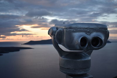 Close-up of coin-operated binoculars against sea during sunset