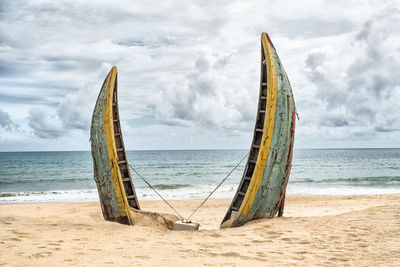 Abandoned boat at beach against cloudy sky