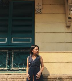 Portrait of young woman looking away against building