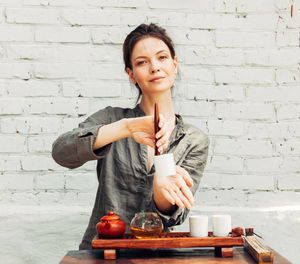 Portrait of young woman making tea against wall