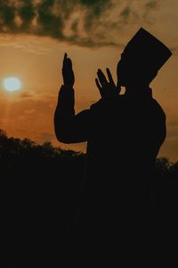 Silhouette man standing by house against sky during sunset