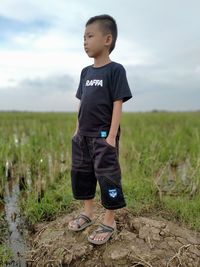 Boy standing on field against sky