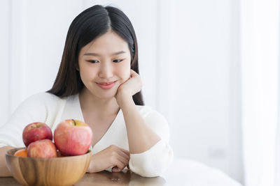 Smiling young woman looking at bowl with fruits on table