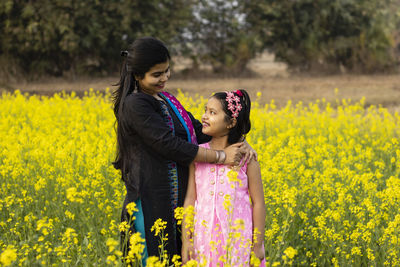 A pretty indian mother and daughter looking at each other and standing in mustard flower field