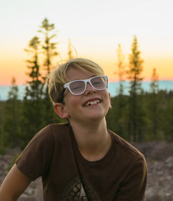 Portrait of smiling boy sitting against sky during sunset