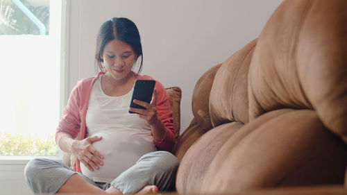 Woman using mobile phone while sitting on sofa