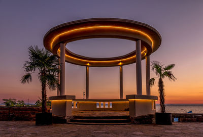 Metallic structure by sea against sky during sunset