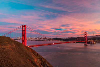 Suspension bridge over river against sky during sunset