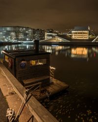 Illuminated bridge over river by buildings against sky at night