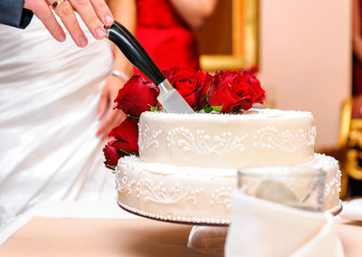 Close-up of hand cutting roses over cake on table