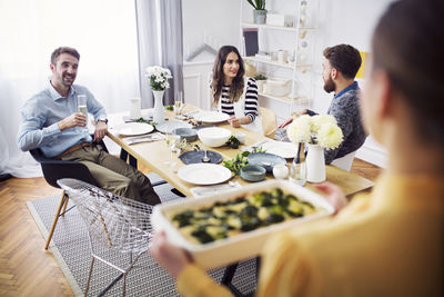 Woman holding serving dish while friends enjoying lunch party at table